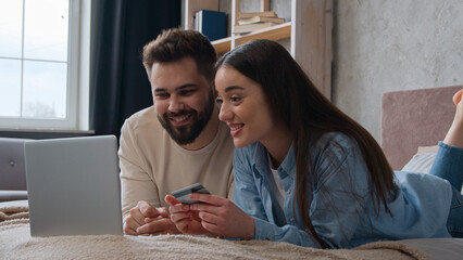 Caucasian couple happy woman and man looking at laptop screen on home bed excited smiling wife and...