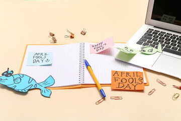 Laptop, notebook, stationery and sticky notes on beige background. April Fools Day prank