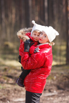 A vertical portrait of a little girl in a red winter jacket embracing her mother. Red, black and white family look winter outfit. 