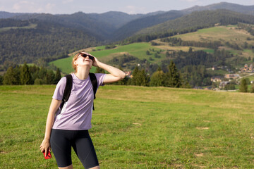 Young beautiful woman in active trekking clothes has headache at the mountains in summer