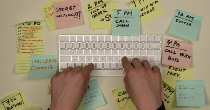 Man typing on keyboard, tasks and to do list appearing on colorful postit papers. Time management and planning concept. Top view, 4K stop motion animation.