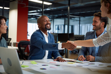 Four multiracial business people in businesswear smiling and shaking hands during meeting in office