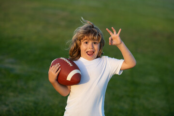 American football, rugby. Kid boy playing with rugby ball in park. Portrait of boy holding american football ball in park. - Powered by Adobe