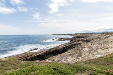 A rocky coastline with greenery, overlooking a vast, serene ocean under a partly cloudy sky.