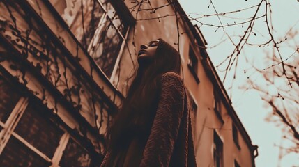 Young woman looking upward, framed by bare branches against a building. - Powered by Adobe