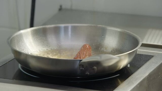 A delicious sausage frying in lots of oil inside of the skillet in the kitchen. Frying the delicious sausage ingredient for hot dogs. Chef rotating the pan frying the delicious sausage.