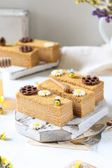 Honey layer cake with bee and daisy decorations on a rustic board.