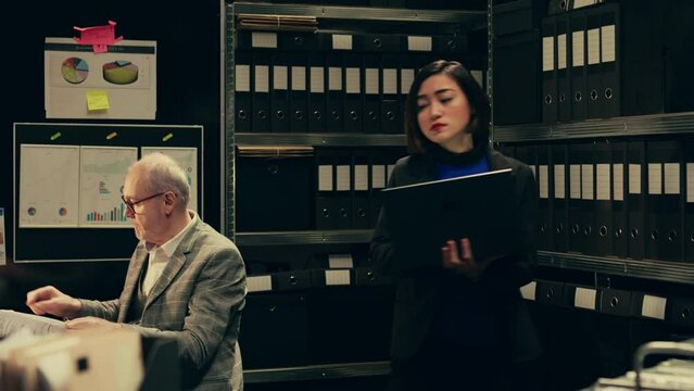 Private investigator organizes archived files for easy access, searching for old file cases to cross reference data. Law enforcement agent looking for classified folders in archive room. Camera B.
