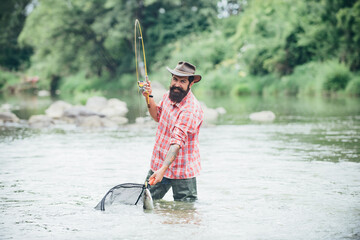 Young bearded man fishing at a lake or river. Flyfishing. Catching trout fish in net.