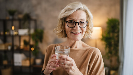 Close up portrait of one mature woman with glass of water at home