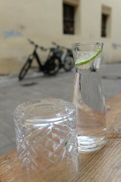 Sprudelndes Mineralwasser mit Limette in einer Karaffe, Wasserglas, im Hintergrund eine Mauer mit Fahrrädern davor. Bayrische Altstadt (Bamberg)