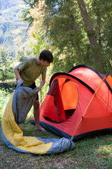 Fototapeta premium A young boy arranges his sleeping bag inside the tent, which is installed in the middle of nature between rivers and mountains.