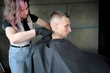 Barber with scissors while cutting hair of man sitting on a chair in barbershop