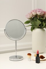 Mirror, cosmetic products and vase with pink roses on white dressing table