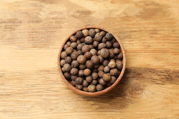 Dry allspice berries (Jamaica pepper) in bowl on wooden table, top view