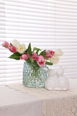 Easter decorations. Bouquet of tulips in vase and bunny figures on white table at home
