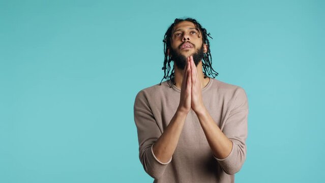 Pious middle eastern man praying to his god, asking for forgiveness, feeling desperate. Spiritual BIPOC man doing worship hand gesturing, confessing, begging for pardon, studio background, camera A