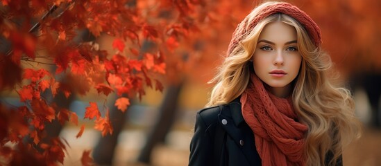A beautiful woman with long blonde hair is seen wearing a vibrant red scarf while standing in a park during the autumn season.