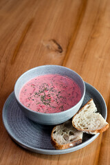 Beetroot soup in a bowl, decorated with herbs, served with a slice of bread.