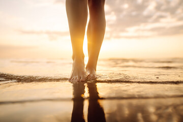 Close- up leg of young woman walking along wave of sea water and sand on the summer beach. Travel,...