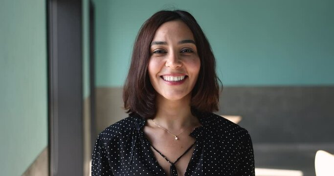 Head shot of young beautiful independent Lebanese businesswoman smile looking at camera standing alone at workplace. Profile of successful employee, promoted or hired worker, university tutor portrait