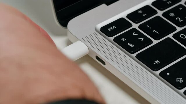 Charging connection to laptop on white table close-up . Phone charging port. USB wire for devices