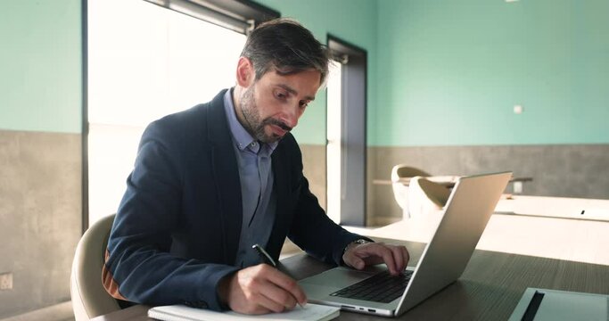 Businessman sit at desk with laptop, noting references for further investigation or analysis, developing strategic plans for business, jotting, create to-do lists to organize his tasks and priorities