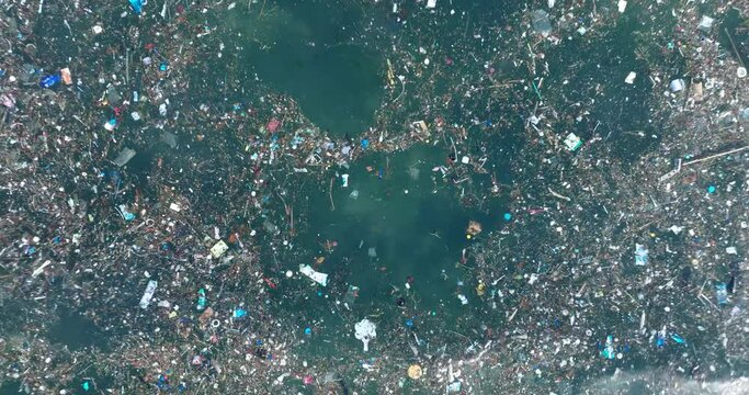 Low altitude top down drone shot of polluted water filled with trash floating over dead coral reef in the turqouise tropical water of Bali Indonesia