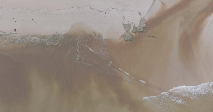 Top down drone shot small shorebreak waves breaking on sand and mixing with muddy river sewage runoff in Bali Indonesia