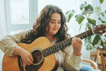 Plus-size young woman enjoying playing guitar in a cozy room. - obrazy, fototapety, plakaty
