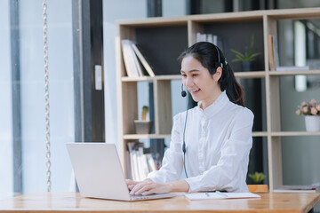 Asian businesswoman using laptop with earphones and working at desk in the office.