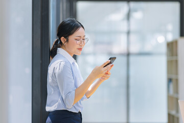 Fototapeta premium Asian businesswoman using smartphone standing at the office. 