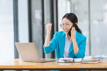 Asian businesswoman wearing a suit using smartphone with digital laptop computer working at modern office, Asian beautiful businesswoman in red suit working in the modern office.