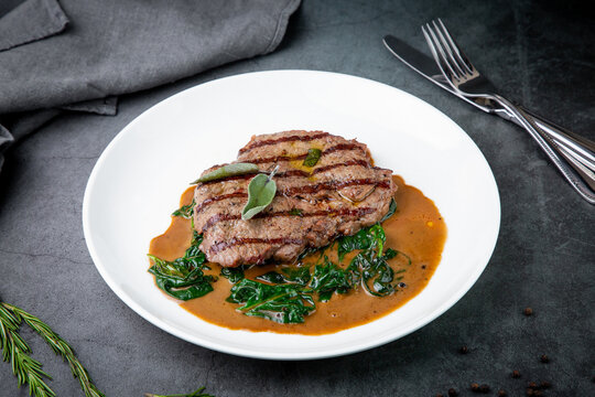 beef steak with gravy and herbs on a white plate