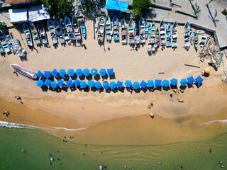 Overhead drone image of the lively Tlacopanocha Beach, showing a line of blue umbrellas and colorful boats in Acapulco