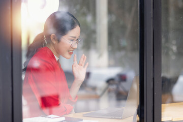 Asian businesswoman making business conference video call on laptop computer sitting at cafe.