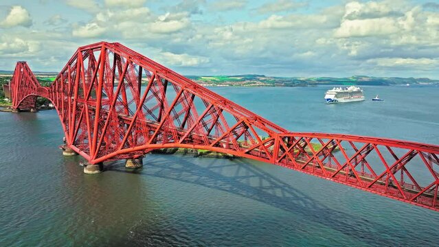 Aerial view of Forth Bridge, a long red railway bridge crossing the Forth estuary. Cantilever railway bridge carrying passengers and freight, cruise ship transporting tourists in Scotland.
