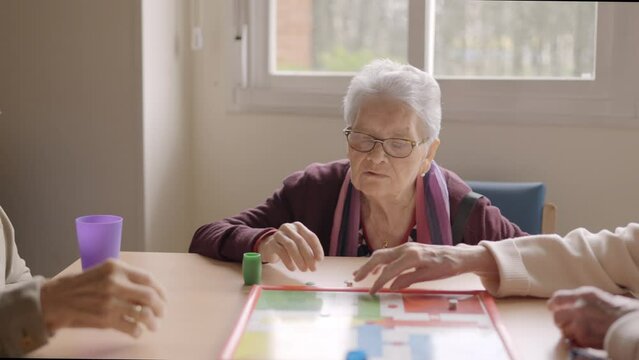 Three old friends playing board game in a nursing home