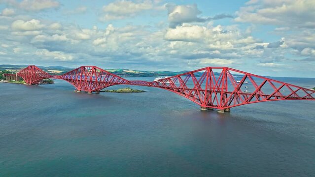 Aerial view of Forth Bridge, a long red railway bridge crossing the Forth estuary. Cantilever railway bridge carrying passengers and freight, cruise ship transporting tourists in Scotland.