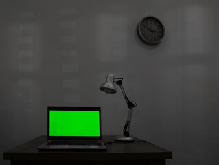 mock up. Laptop with blank green screen, and office on wooden desk. Blank computer monitor on wood table with lamp light. isolated on white wall background. mockup. night evening scene. clock on wall