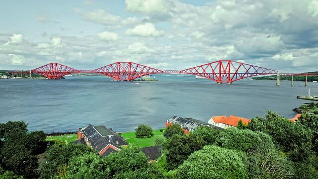 Aerial view of Forth Bridge, a long red railway bridge crossing the Forth estuary. Cantilever railway bridge carrying passengers and freight, cruise ship transporting tourists in Scotland.