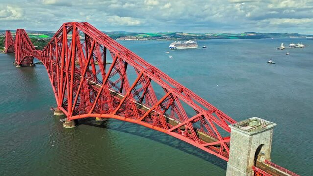 Aerial view of Forth Bridge, a long red railway bridge crossing the Forth estuary. Cantilever railway bridge carrying passengers and freight, cruise ship transporting tourists in Scotland.