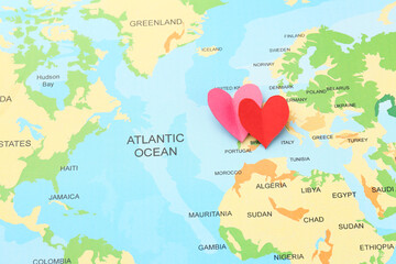 Fototapeta premium Honeymoon concept. Two red paper hearts on world map, top view