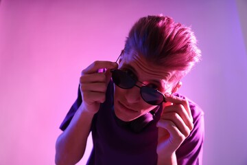 Young man with sunglasses on pink background in neon lights