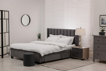 Stylish bedroom interior with large bed, chest of drawers and lamp