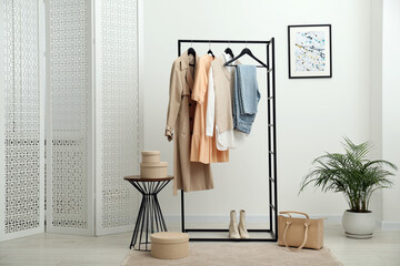 Rack with different stylish women's clothes, boots, bag and green houseplant indoors