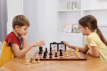 Cute children playing chess at table in room - Powered by Adobe