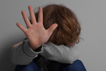 Child abuse. Boy making stop gesture near grey wall, selective focus