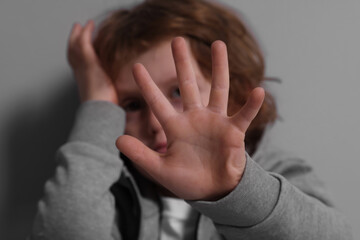 Child abuse. Boy making stop gesture near grey wall, selective focus