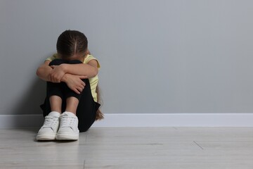 Child abuse. Upset girl sitting on floor near grey wall, space for text